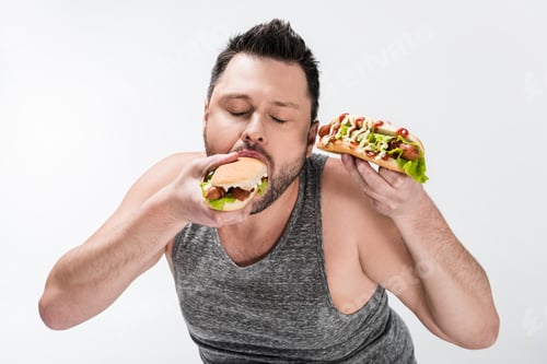 Preview: overweight man in tank top eating tasty hot dog isolated on white