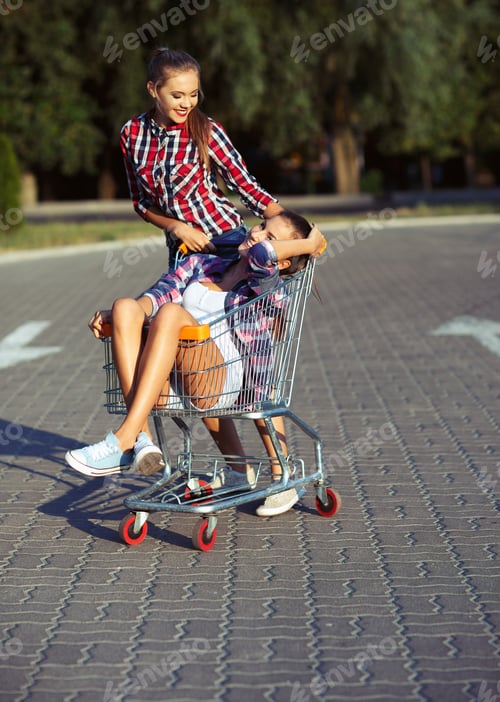 Preview: Two happy beautiful teen girls driving shopping cart outdoors