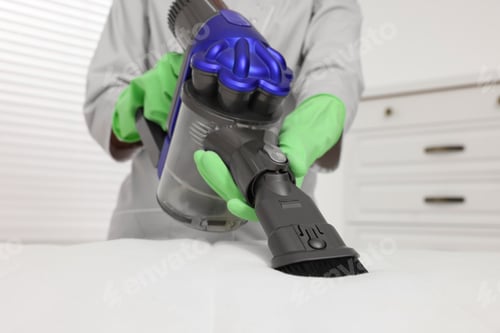 Preview: Woman in gloves disinfecting mattress with vacuum cleaner indoors, closeup