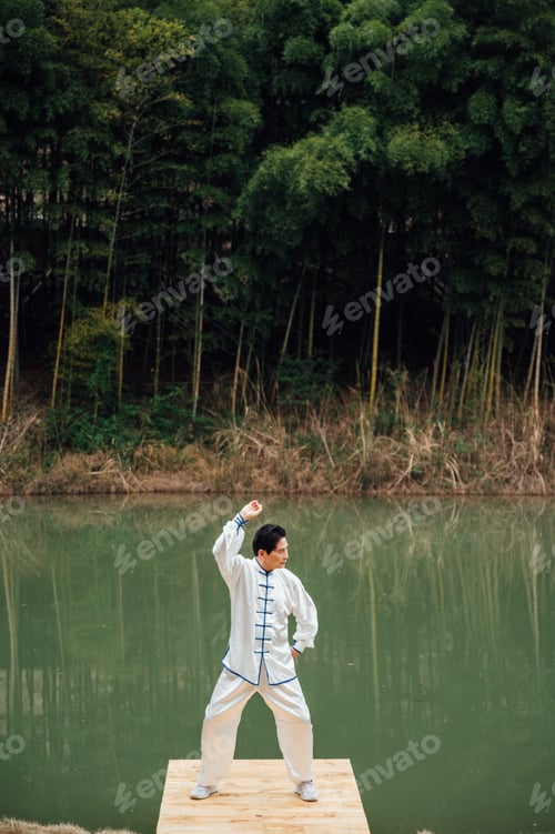 Preview: Asian senior man practicing tai chi outside by the river