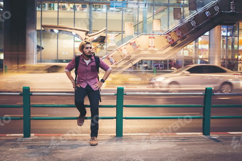 Preview: Hipster bearded man sitting on railing with car motion background while traveling at night.