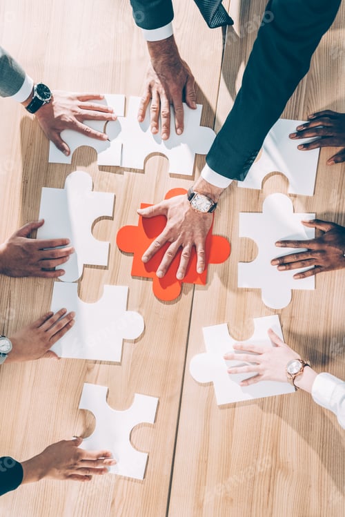 Preview: overhead view of multiracial businesspeople assembling puzzle on table