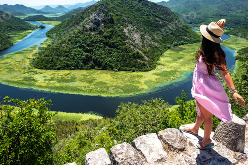 Preview: high angle view of woman in pink dress and hat standing near Crnojevica River in Montenegro