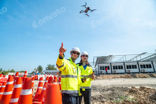 Preview: Two engineers in high visibility jackets and helmets operate a drone