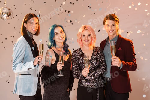 Preview: joyful nonbinary people with champagne glasses looking at camera while celebrating christmas on