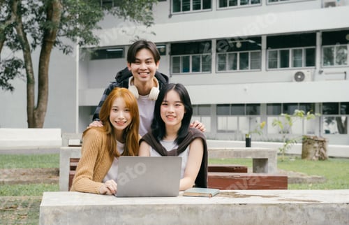 Preview: Group of cheerful asian students collaborating outdoors on campus, using a laptop for studying toget