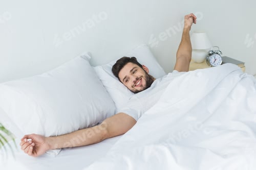 Preview: happy bearded man stretching in bed in the morning