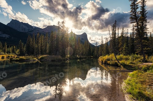 Preview: Sunset over rocky mountain with pine forest reflection on pond in Canmore
