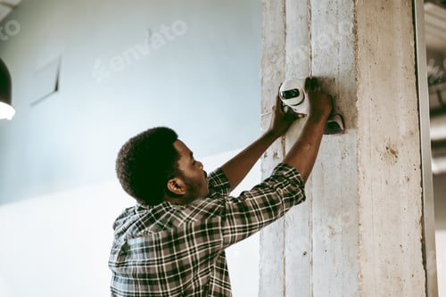 Preview: Skilled worker installing security camera on concrete pillar in modern workspace in the afternoon