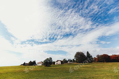Preview: Landscape of green fields, private houses in distance, beautiful clouds in sky
