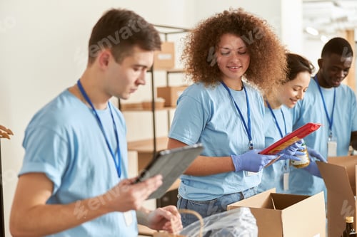 Preview: Young woman in protective gloves sorting, packing foodstuff in cardboard boxes, volunteering