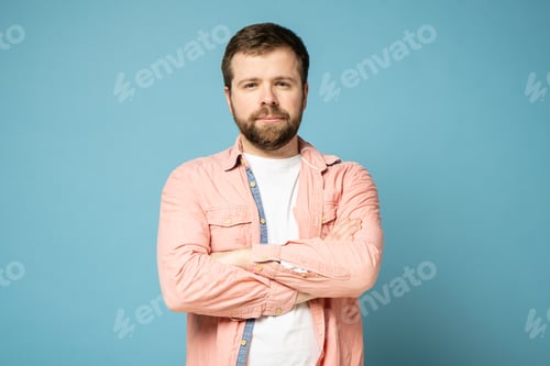 Preview: Calm, bearded man stands confidently with arms crossed and stares intently at the camera