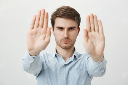 Preview: Studio shot of handsome serious young man in ordinary clothes pulling palms towards camera in stop