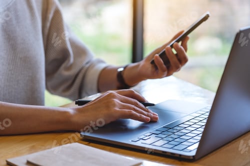 Preview: Closeup image of a woman holding and using mobile phone and laptop computer in office