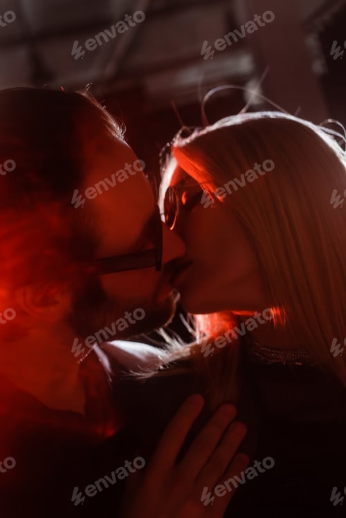 Preview: Low angle view of couple in sunglasses kissing during party with lighting