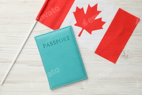 Preview: Passport in light blue cover and flag of Canada on wooden table, top view