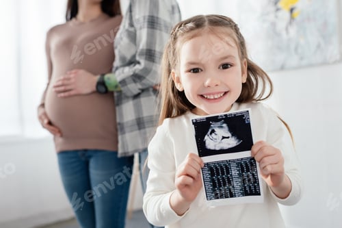 Preview: Selective focus of smiling kid holding ultrasound scan of baby near mom embracing pregnant woman at