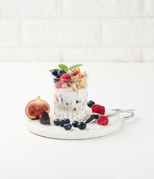 Preview: Transparent glass with granola poured with yogurt, on top of ripe raspberries