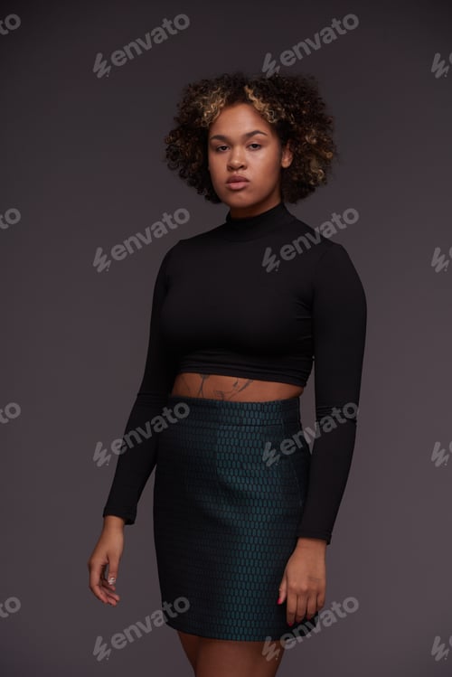 Preview: Young serene fashion model in cropped top and mini skirt looking at camera