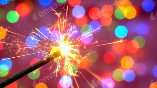 Preview: Bright burning sparkler against the backdrop of defocused multicolored garland. Blurred backdrop.