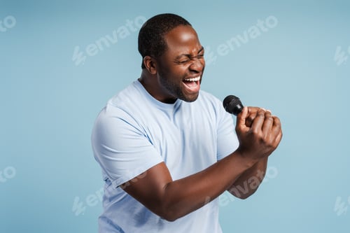 Preview: Young African American man having fun, singing favorite song, holding microphone in studio