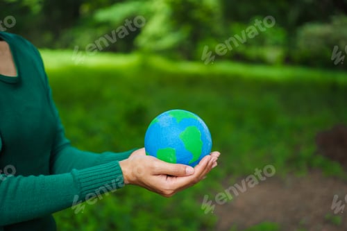 Preview: An Asian woman holds a globe in green forest,symbolizing importance preserving nature.emphasizes