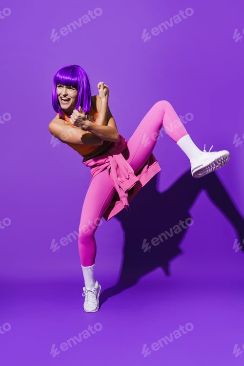 Preview: Carefree woman dancer wearing colorful sportswear performing against purple background