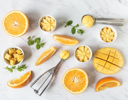Preview: Orange and mango sorbet in bowl and in ice cream spoons and fruits spices on marble background.