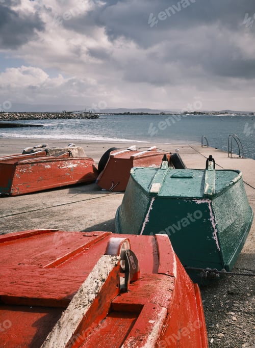 Preview: Vertical shot of old red and green inverted boats on the coast under the cloudy sky