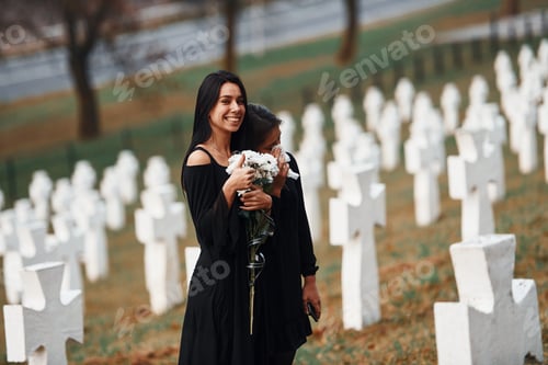 Preview: Two young women in black clothes visiting cemetery with many white crosses
