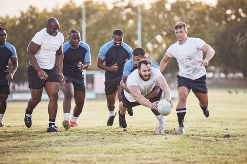 Preview: Caucasian rugby player diving to score a try during a rugby match outside on a field. Young male at