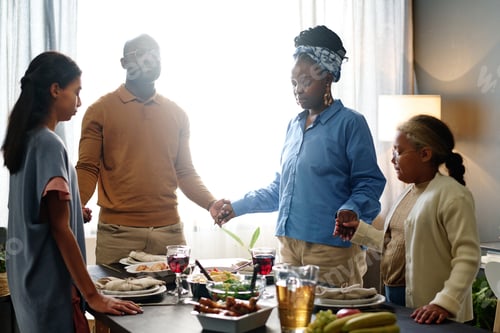 Preview: Young family of four holding by hands while standing around served table