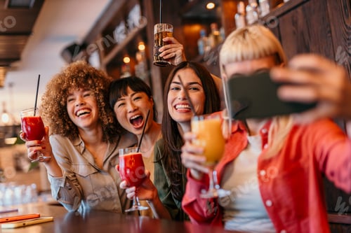 Preview: Cheerful friends taking selfie while drinking cocktails at the bar