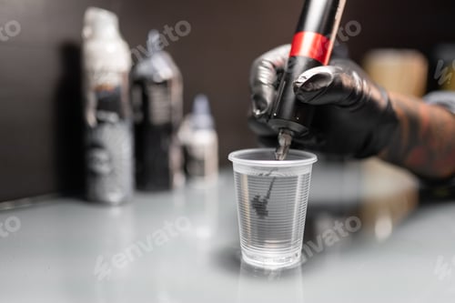 Vista previa: Close up of a tattoo artist is pouring ink into a plastic glass to clean the needle