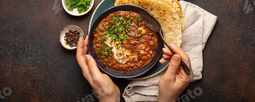 Preview: Female hands holding a bowl and eating traditional Indian Punjabi dish Dal makhani with lentils and
