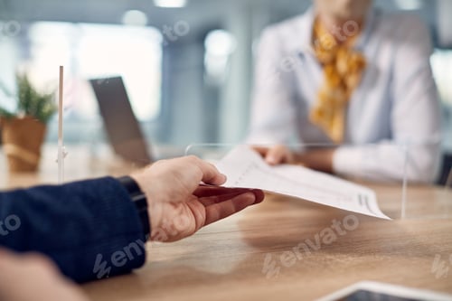 Preview: Close-up of colleagues passing documents through sneeze guard due to coronavirus pandemic.