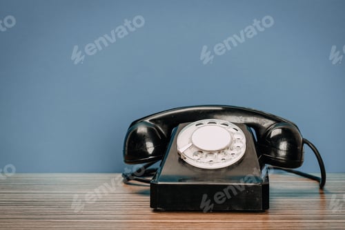 Preview: Old rotary phone placed on wooden table with blue wall in the background