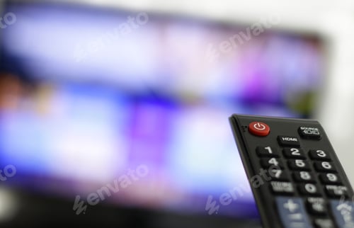 Preview: Closeup shot of a person holding a black remote control in front of the TV