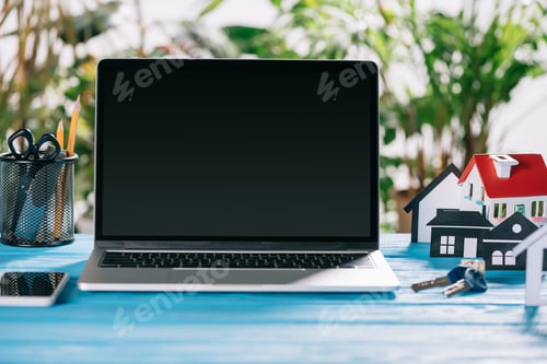 Preview: selective focus of smartphone, laptop with blank screen and keys near paper houses on wooden desk,