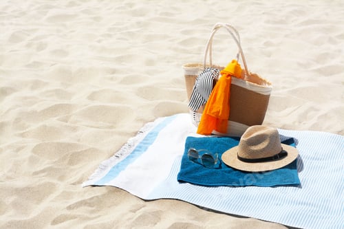 Preview: Blue blanket with towel, bag and beach accessories on sand. Space for text
