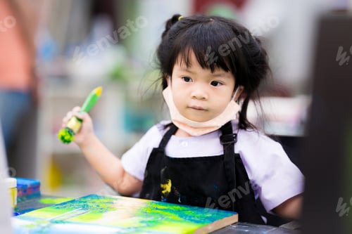 Preview: A 4 year old pupil is studying art in a class. Child wearing a black apron uniform.