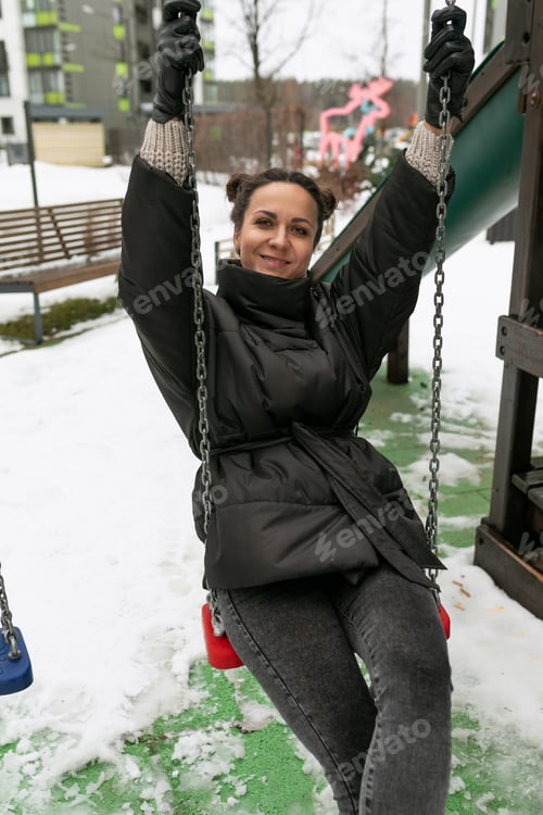 Preview: Young pretty woman in a winter jacket fooling around on the playground