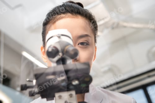 Preview: partial view of woman scientist looking through microscope on reagents in laboratory