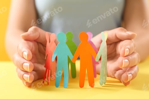 Preview: Woman protecting paper human figures on yellow table, closeup. Diversity and inclusion concept