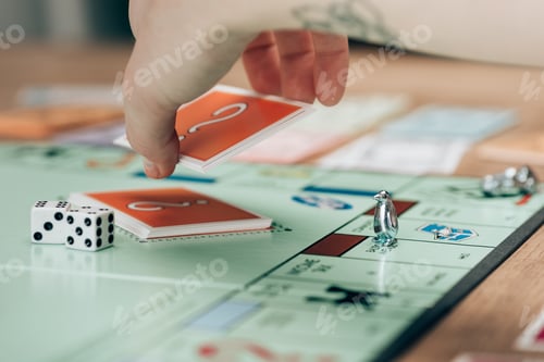 Preview: KYIV, UKRAINE - NOVEMBER 15, 2019:Cropped view of woman holding card by dices on monopoly game