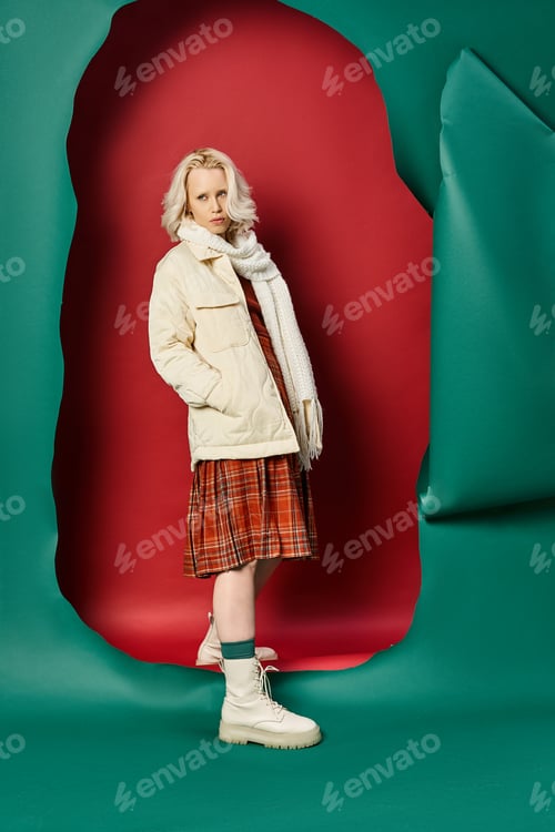 Preview: full length of blonde woman in stylish winter outfit posing on red with turquoise background