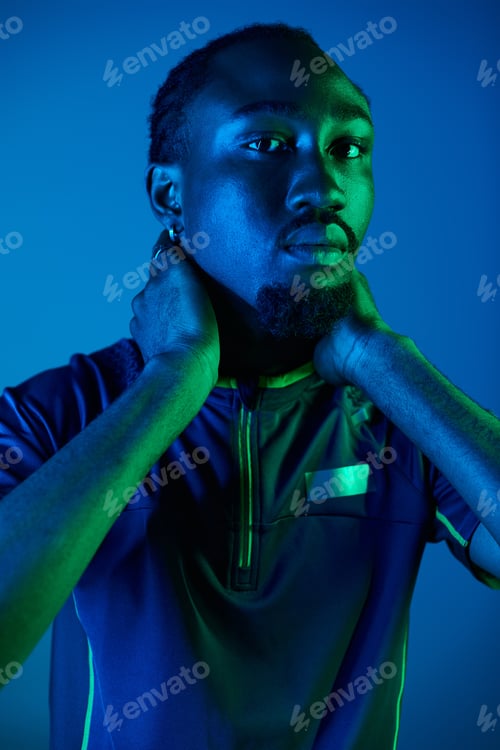 Preview: Young African American man poses confidently in stylish attire against neon studio backdrop