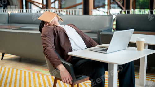 Preview: Brown suit asian man is leaning on the chair with face covered with book. Getting tired or sleepy.