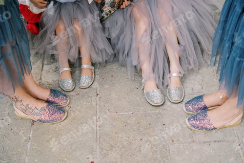 Preview: Bridesmaids and flower girls stand on the paving stones in sandals. Cropped. Faceless
