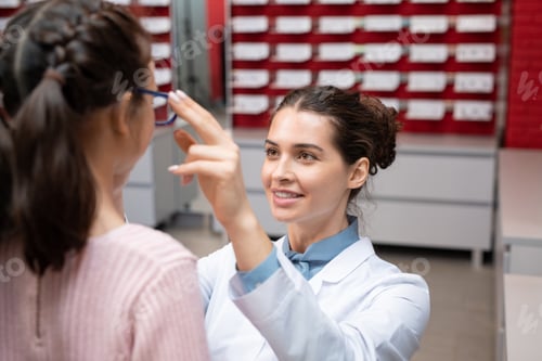 Preview: Happy young female ophthalmologist in whitecoat looking at little patient